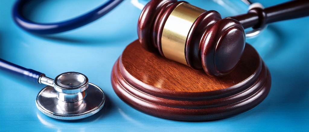 Un mazo de juez de madera descansa junto a un estetoscopio sobre una superficie azul, simbolizando la intersección de la ley y la medicina.