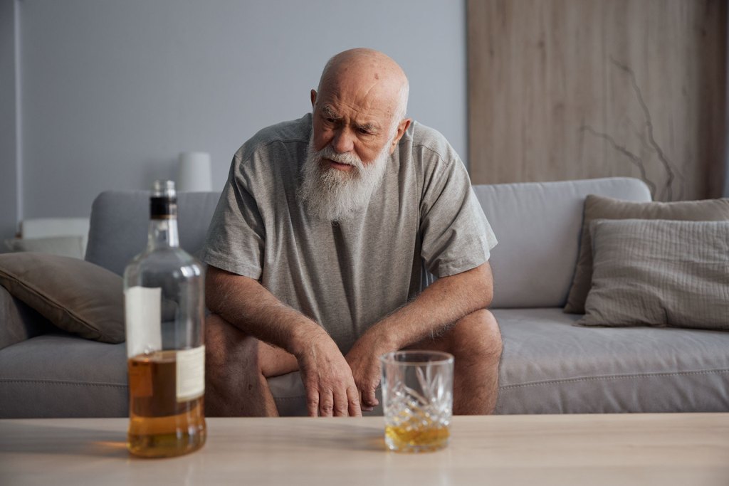 Hombre mayor de edad sentado en un sofá con alcohol
